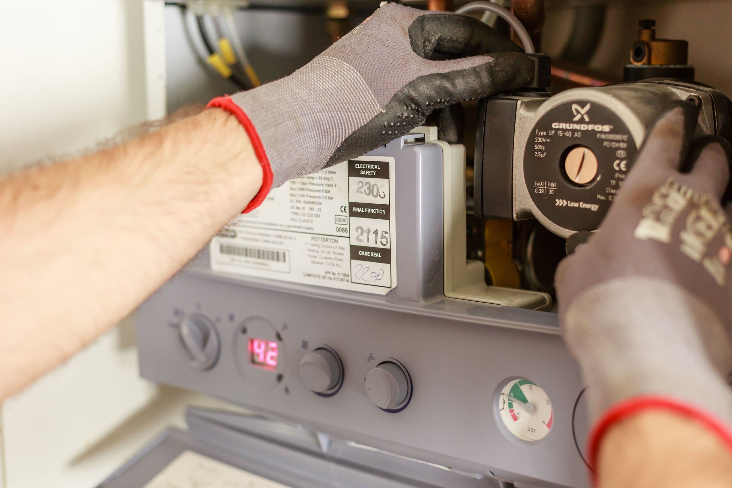 An engineer's gloved hands servicing the pump inside a domestic gas boiler